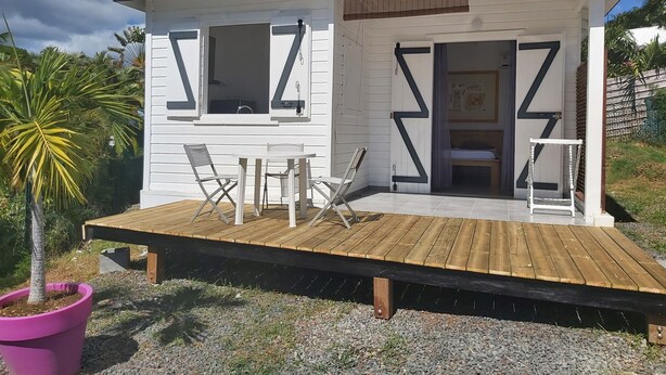 Eine kleine, weiße Holzhütte mit einer Holzterrasse, zwei Stühlen und einem Tisch.