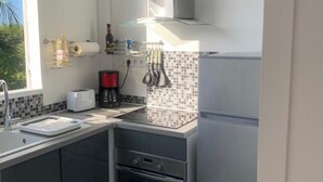 Eine kompakte Küche mit Einbauofen, Mikrowelle und Kühlschrank. Ein Fenster sorgt für natürliches Licht, und die Küche verfügt über eine geflieste Spritzschutzleiste und dunkle Küchenschränke.