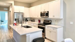 A modern kitchen with white cabinetry, stainless steel appliances, and a central island with a sink. - SWFL: Lake McGregor 3 bedroom Home - Entire Home! (Fort Myers)