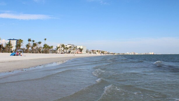 A beach with a hotel, palm trees, and ocean waves. - SWFL: Lake McGregor 3 bedroom Home - Entire Home! (Fort Myers)