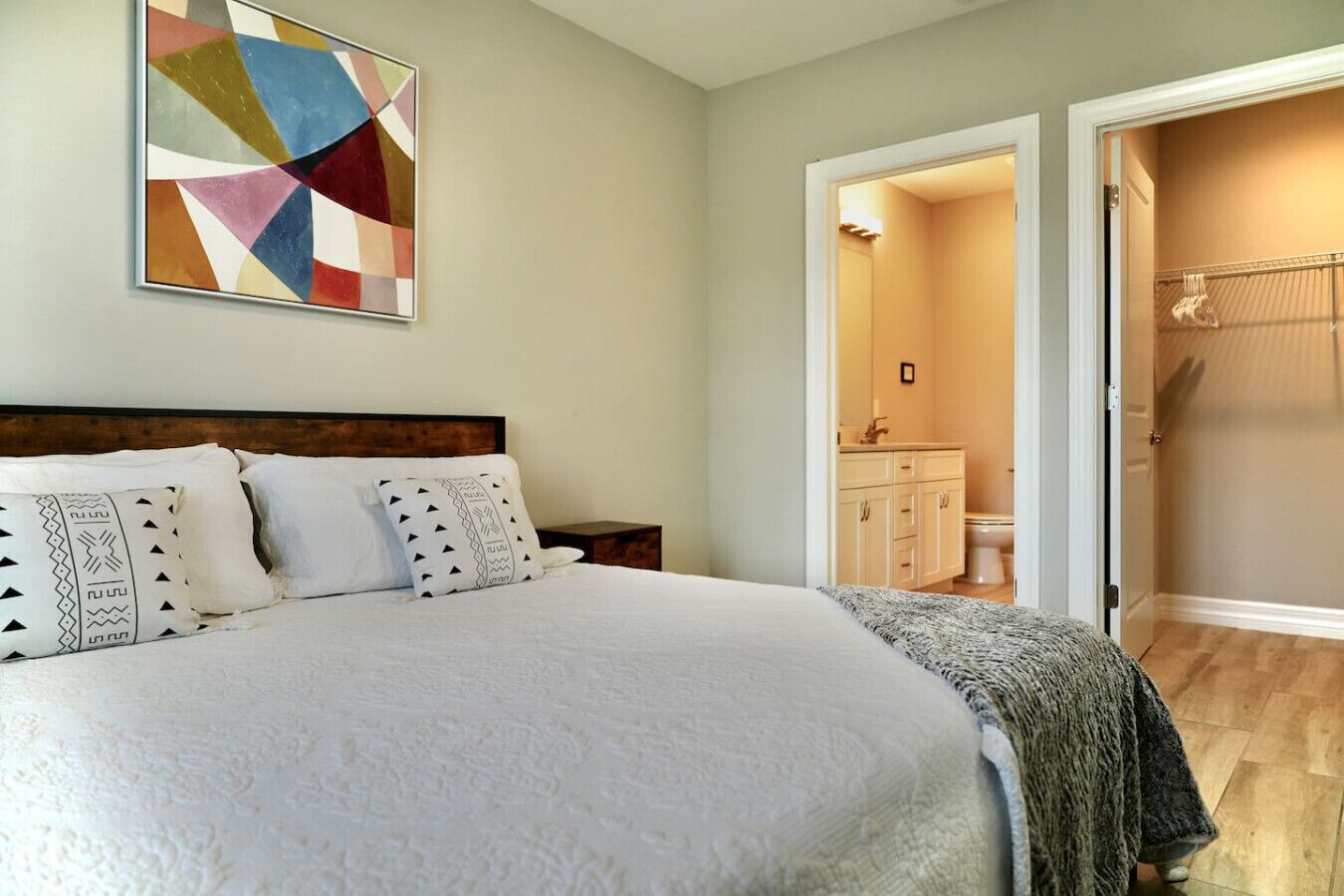 A bedroom with a large bed, a bedside table, a nightstand, a bathroom with a toilet and sink, and a walk-in closet.