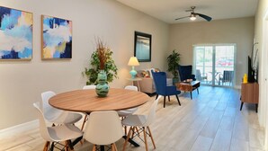A modern living room with a round wooden table, white chairs, a blue armchair, a floor lamp, and a ceiling fan. - SWFL: Lake McGregor 3 bedroom Home - Entire Home! (Fort Myers)
