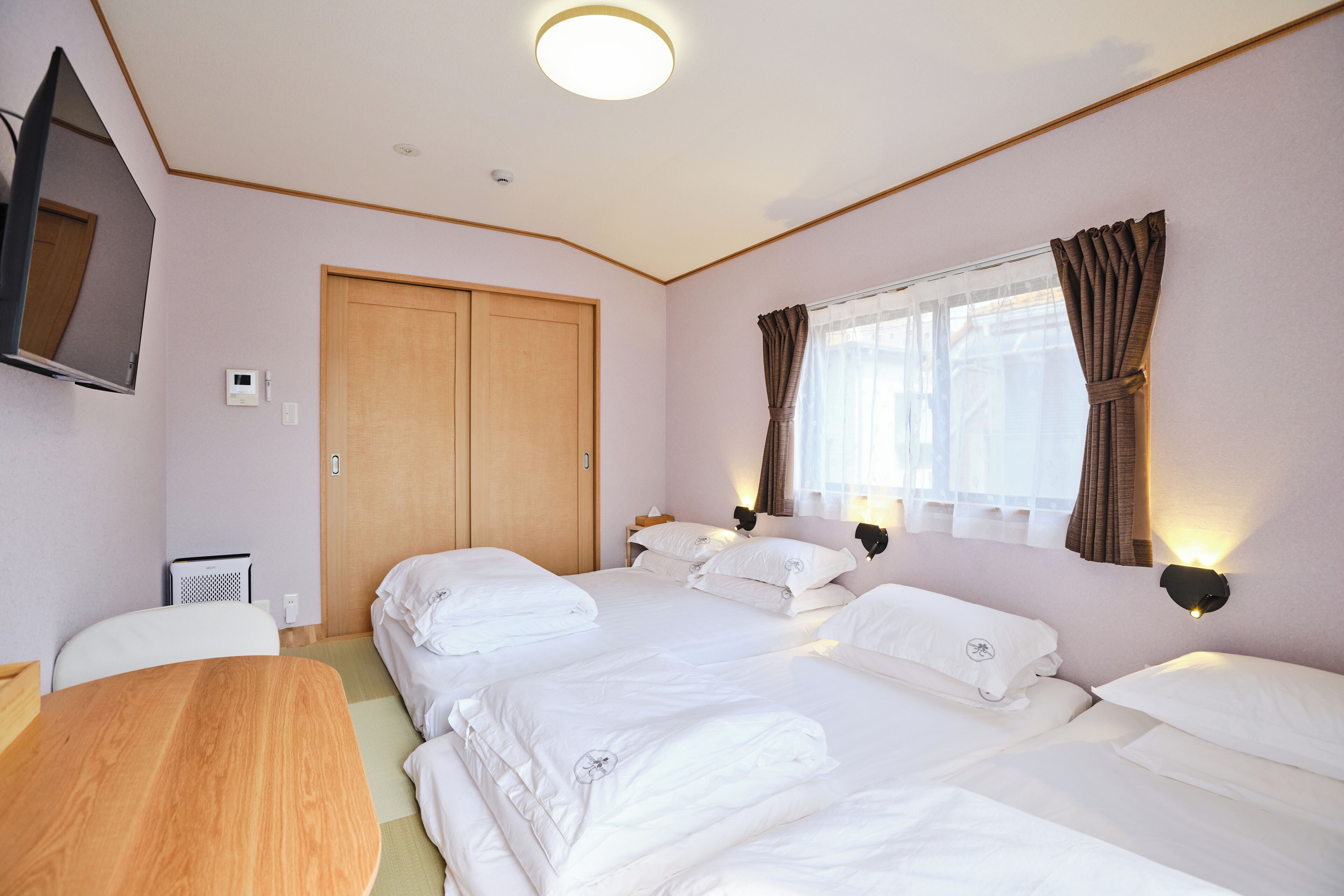 A hotel room with two beds, a wooden desk, a television, and a window with curtains.
