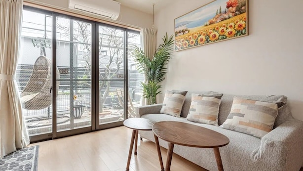 Un salon comprenant un canapé, une petite table, un fauteuil suspendu et une grande fenêtre donnant sur un jardin.