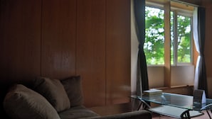 A room with a wooden panel wall, a glass-top table with a book and a remote control, and a window with curtains. - STARRY SKY COTTAGE 12 (Kitami)