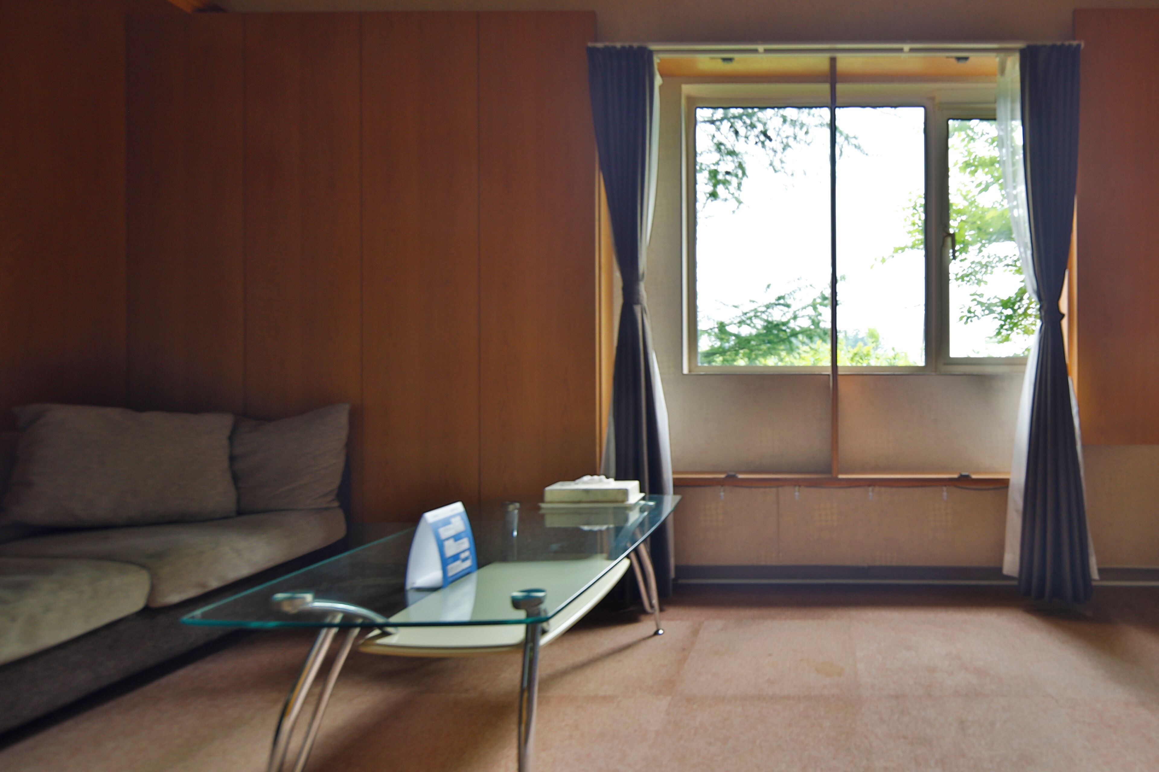 A room with a glass table, a sofa, and a window with curtains.