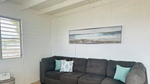 A sectional sofa with two pillows, a framed picture on the wall, and a small round table with a sign.