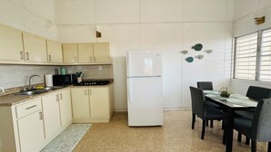A kitchen with white cabinets, a white refrigerator, a dining table with chairs, and a window with blinds.