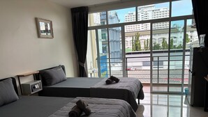 Une chambre d’hôtel avec deux lits, une petite table de chevet avec une lampe, un tableau encadré au mur et une vue sur la ville à travers de grandes fenêtres.