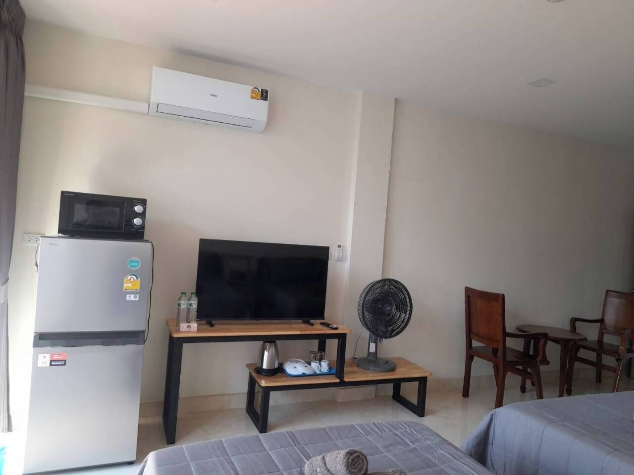 Egy szállodai szoba, amelyben található egy síkképernyős televízió, egy hűtőszekrény, egy mikrohullámú sütő, egy ventilátorral felszerelt faasztal és két fa szék.