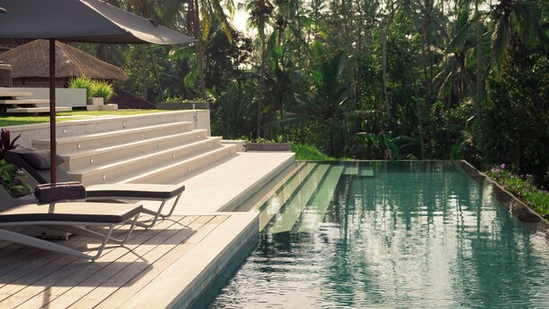 A poolside area with a lounge chair and umbrella, surrounded by palm trees and a staircase leading to a building. - Private Villa with butler service surrounded by rice fields and jungle views. (KAB. GIANYAR)