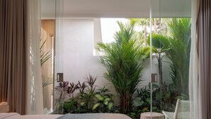 A modern bedroom with a large bed, a glass door leading to a balcony with lush greenery. - Private Villa with butler service surrounded by rice fields and jungle views. (KAB. GIANYAR)