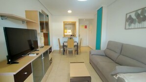 A modern living room with a flat-screen TV, a sofa, a coffee table, and a dining area with chairs and a table. - ACV - Torremar-2ª Linea Planta 3 Sur (OROPESA)