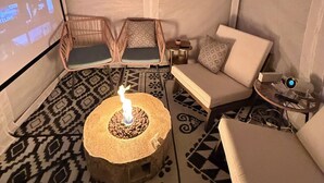 A cozy tented room with two wicker chairs, a cushioned sofa, a small table with a candle, and a projector screen displaying a video. - Cozy Cottage in Sacramento with Fire Pit & Backyard Movie Nights (Sacramento)