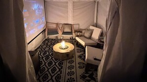 A cozy tented room with a fire pit, two chairs, a sofa, and a projection screen displaying a movie. - Cozy Cottage in Sacramento with Fire Pit & Backyard Movie Nights (Sacramento)