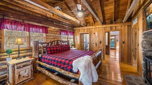 A log cabin bedroom with a bed, a nightstand, a lamp, a ceiling fan, and a fireplace. - 4 Private Cabins•16 Acres•Hot Tubs•Sauna•Near UTK (Knoxville)