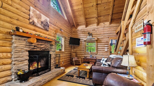 A log cabin interior with a stone fireplace, leather furniture, a television, and a bear feeding sign. - 4 Private Cabins•16 Acres•Hot Tubs•Sauna•Near UTK (Knoxville)