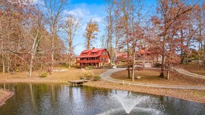A lakeside view with a red house, a dock, and a fountain. - 4 Private Cabins•16 Acres•Hot Tubs•Sauna•Near UTK (Knoxville)