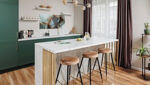 A modern kitchen with a marble countertop, green cabinets, and a bar area with stools. - DA-LI Residence - AC and Netflix (Brașov)