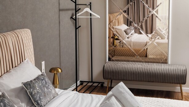 A modern bedroom with a bed, bedside table, lamp, hanging clothes rack, bench, and a large mirror reflecting the room. - DA-LI Residence - AC and Netflix (Brașov)