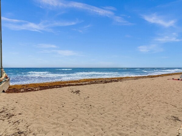 A sandy beach with a clear blue sky and ocean waves.