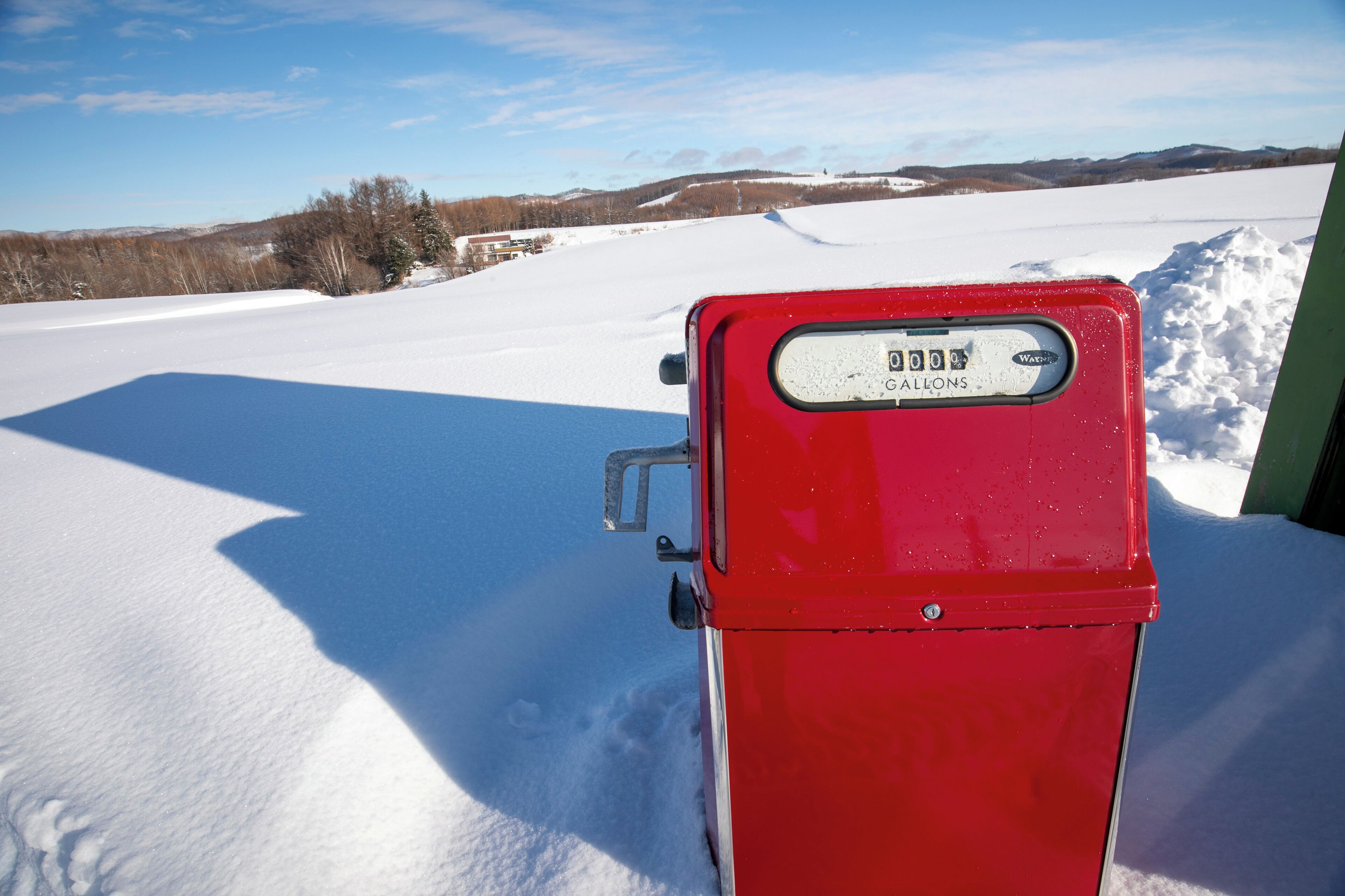 Une pompe à essence rouge se dresse dans un paysage enneigé, sous un ciel dégagé.
