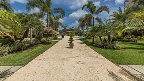 A pathway lined with palm trees and a building in the background. - Amazing 3BR Eagle Beach Condo @LeVent  Pool  GYM (Noord)