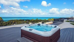 Un bain à remous sur une terrasse en bois, avec vue sur l’océan et un ciel dégagé.