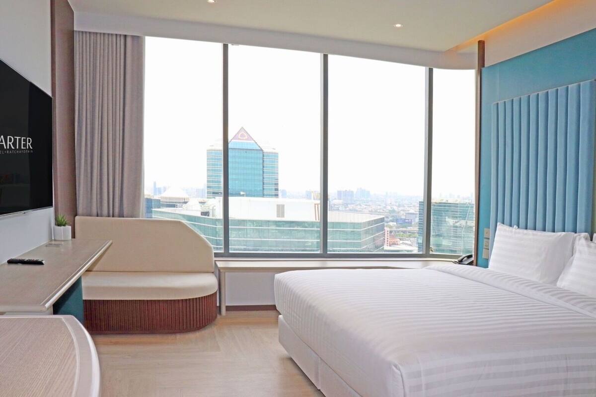 Una habitación de hotel con un ventanal grande, una cama, un escritorio y una zona de estar.