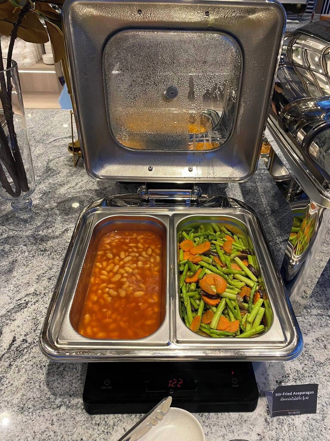 A buffet with two dishes: baked beans and stir-fried asparagus.
