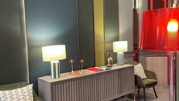 Un vestíbulo de hotel moderno con una mesa consola central, dos sillones, un espejo grande y una lámpara roja.
