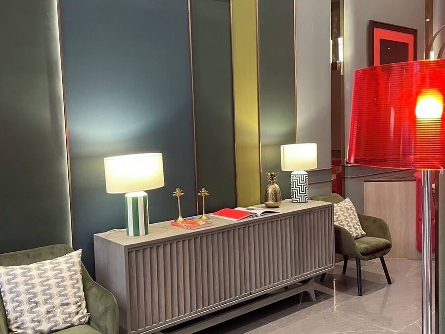 Un vestíbulo de hotel moderno con una mesa consola central, dos sillones, un espejo grande y una lámpara roja.