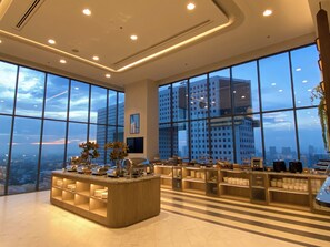 A modern hotel lobby with large windows offering city views, a central reception desk, and a clean, well-lit interior. - The Quarter Ratchayothin by UHG (Bangkok)