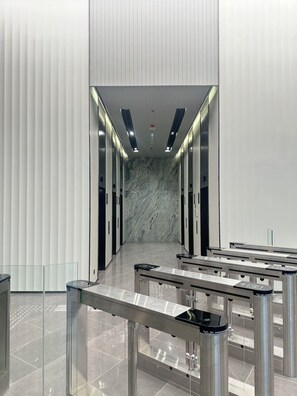 A modern elevator lobby with a marble wall, metal railings, and a glass partition. - The Quarter Ratchayothin by UHG (Bangkok)
