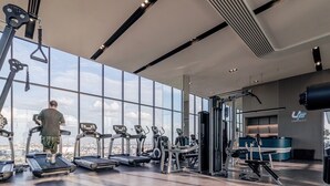 A gym with treadmills, weight machines, and a large window overlooking a cityscape. - The Quarter Ratchayothin by UHG (Bangkok)