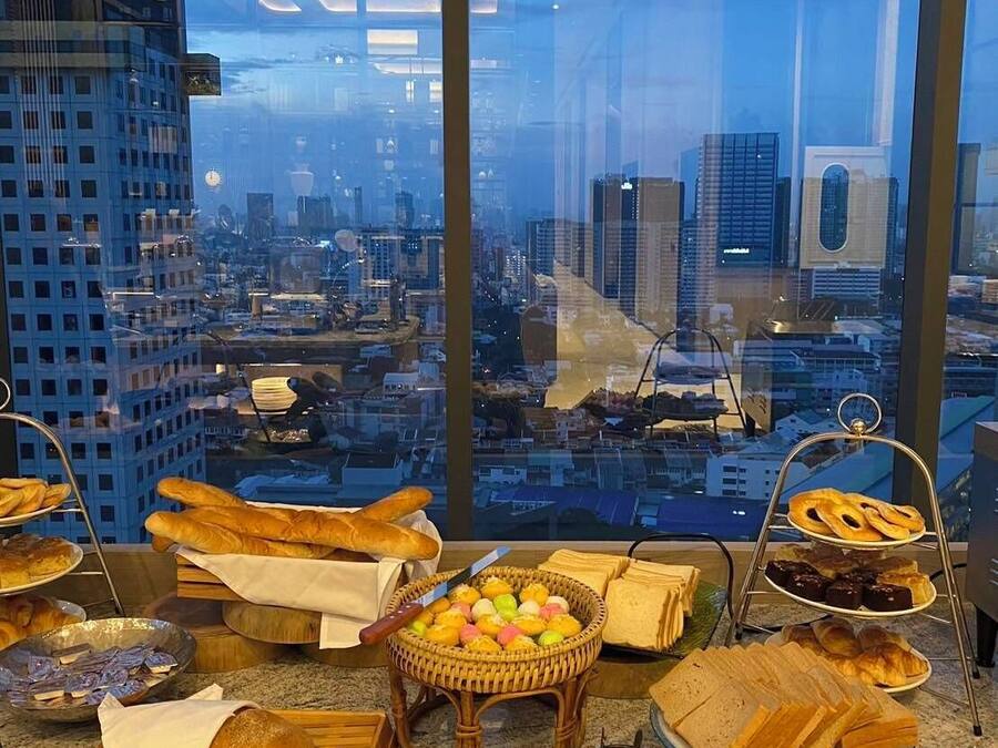 A breakfast buffet with various pastries and bread, set against a cityscape view through large windows.