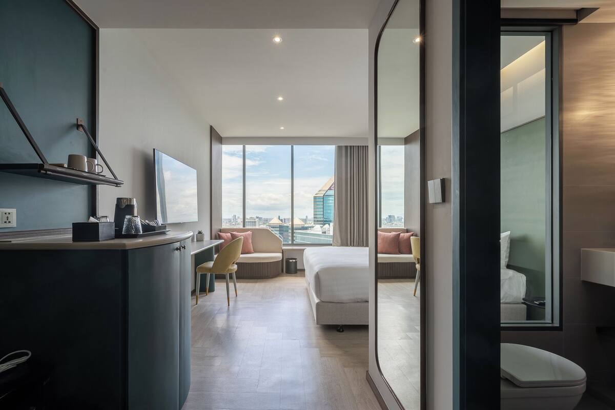 Una habitación de hotel moderna con escritorio, cama, sofá y un amplio ventanal con vistas a la ciudad.