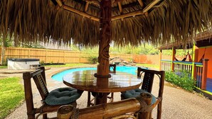 A thatched-roof outdoor seating area with a pool in the background. - Modern, exotic 5br, pool, hot-tub near Woodlands (Spring)