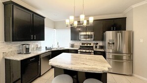 A modern kitchen with dark cabinets, stainless steel appliances, a marble island, and pendant lighting. - Modern, exotic 5br, pool, hot-tub near Woodlands (Spring)
