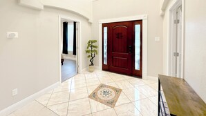 A hallway with a red door, a potted plant, and a tiled floor. - Modern, exotic 5br, pool, hot-tub near Woodlands (Spring)