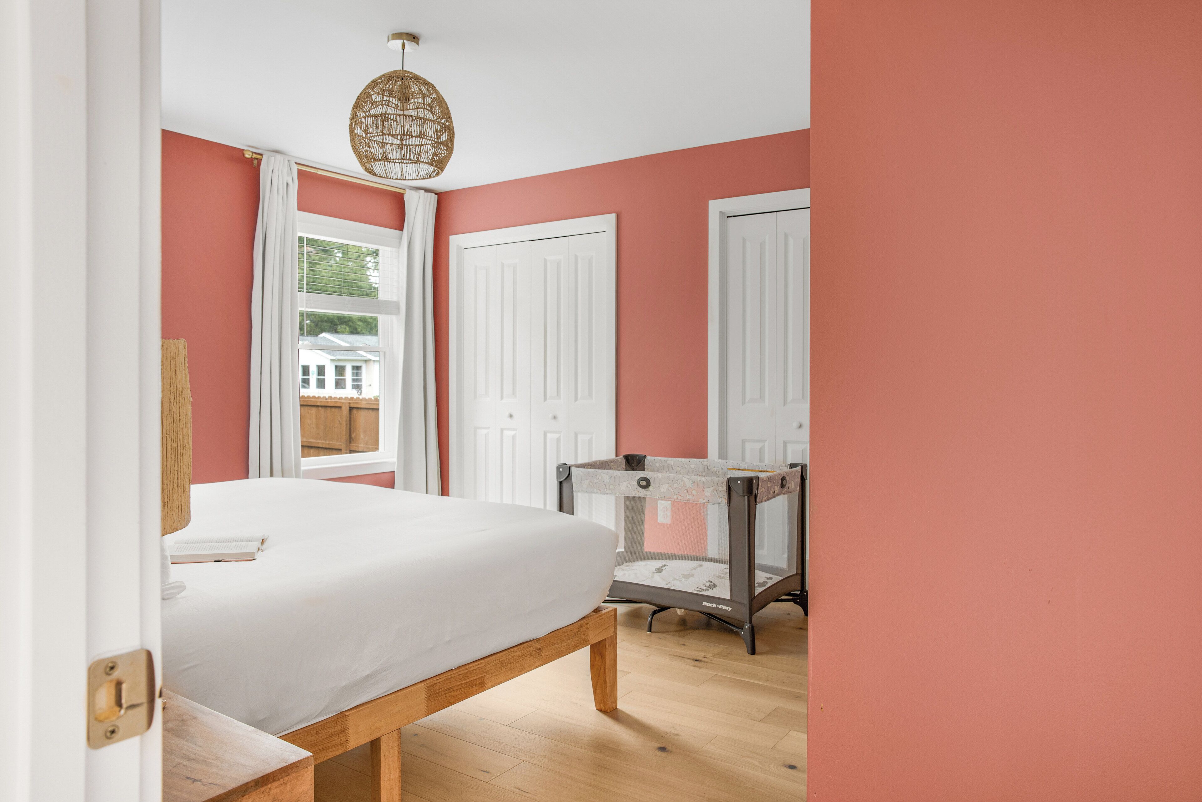 A bedroom with a bed, a window with curtains, a door, and a hanging light fixture.