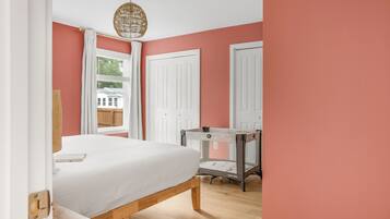 A bedroom with a bed, a window with curtains, a door, and a hanging light fixture.