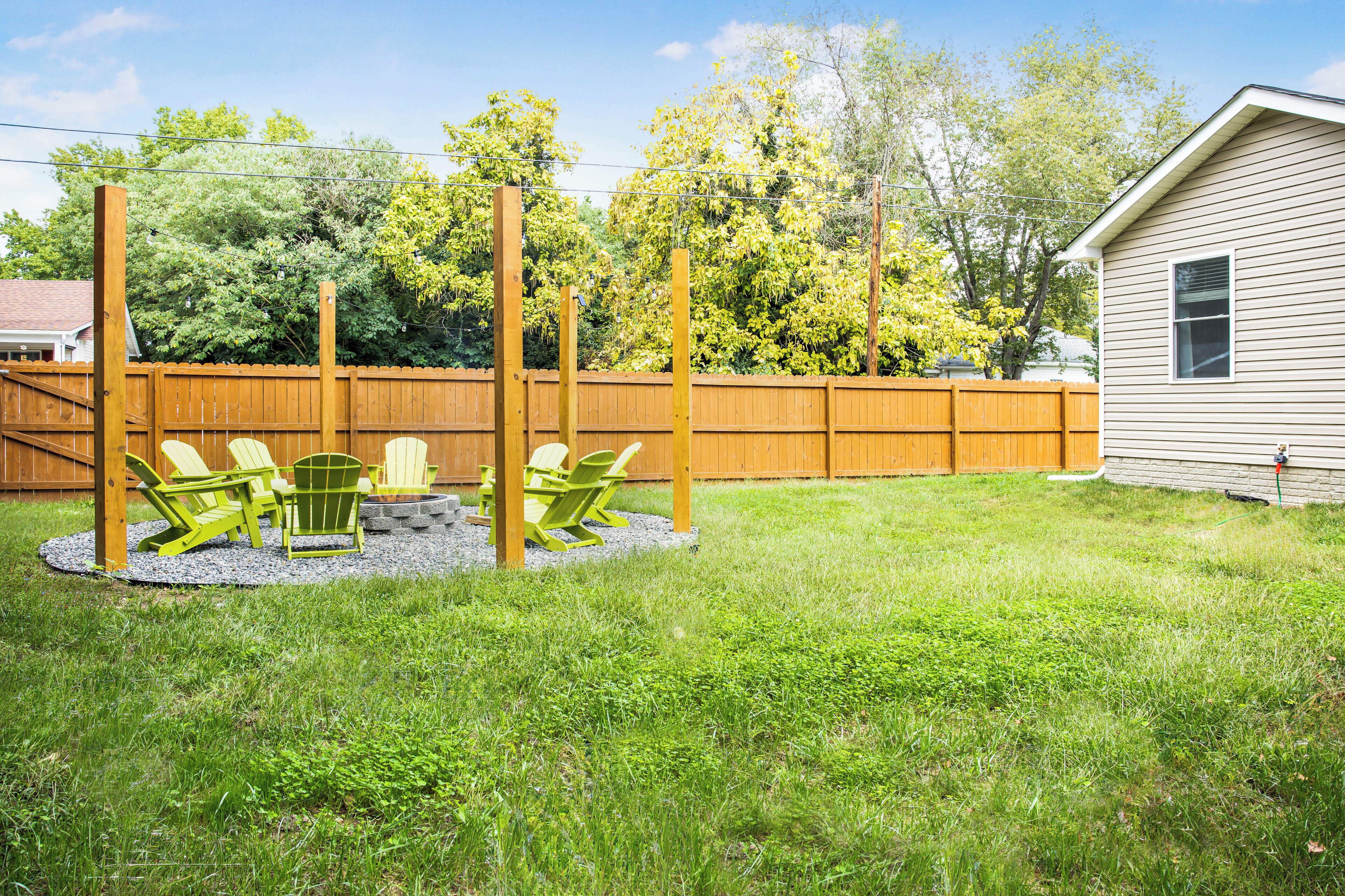 A backyard with a wooden fence, a swing set, and green Adirondack chairs.