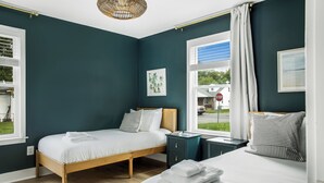 Un dormitorio con dos camas, una ventana con vistas, una señal de stop en el exterior y un cuadro enmarcado en la pared.