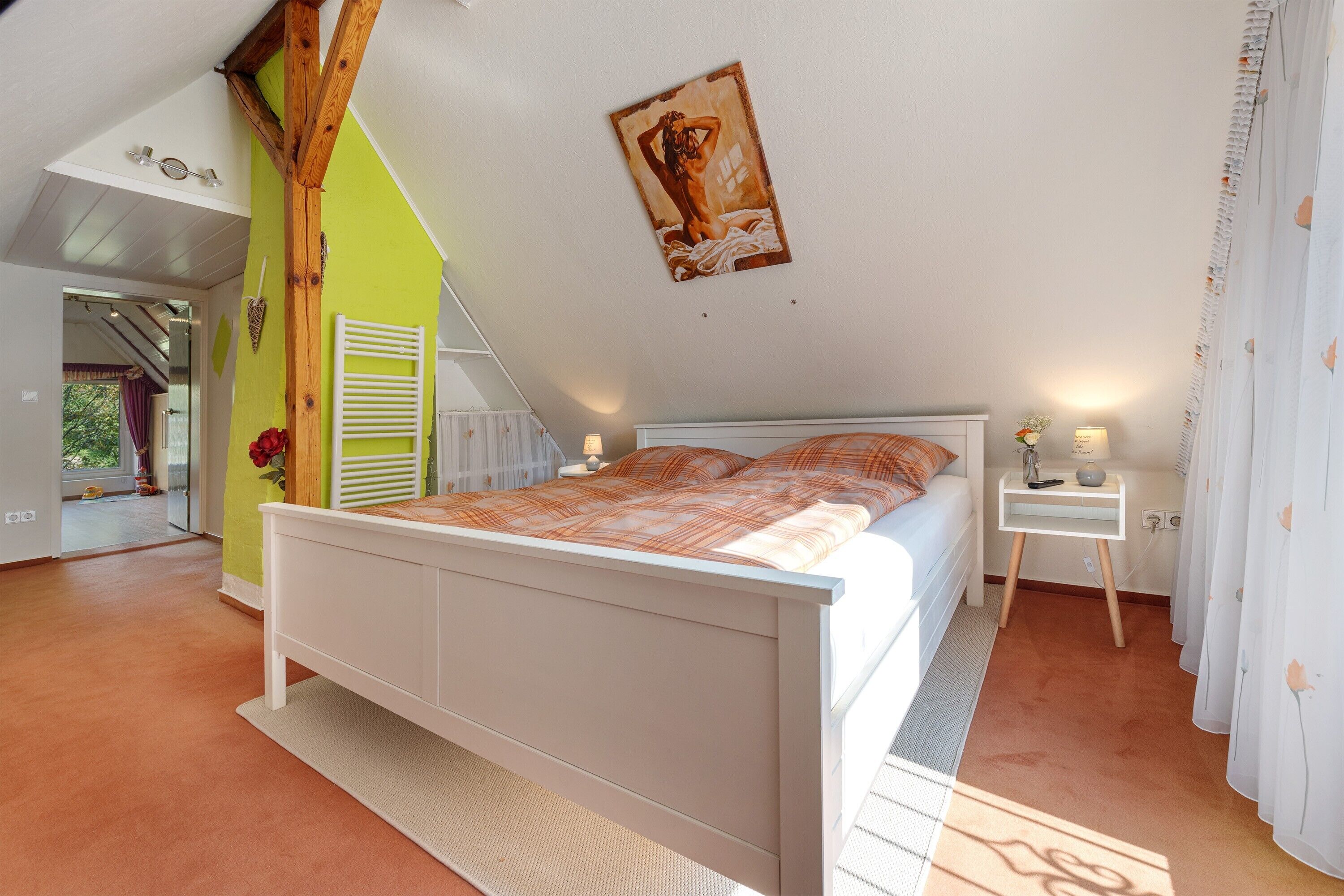 Een slaapkamer met een schuine kap, een bed, een nachtkastje en een raam met gordijnen.