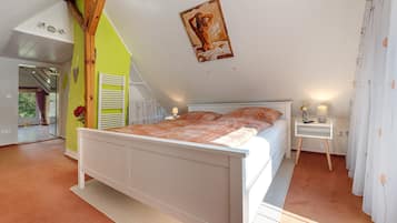 Een slaapkamer met een schuine kap, een bed, een nachtkastje en een raam met gordijnen.