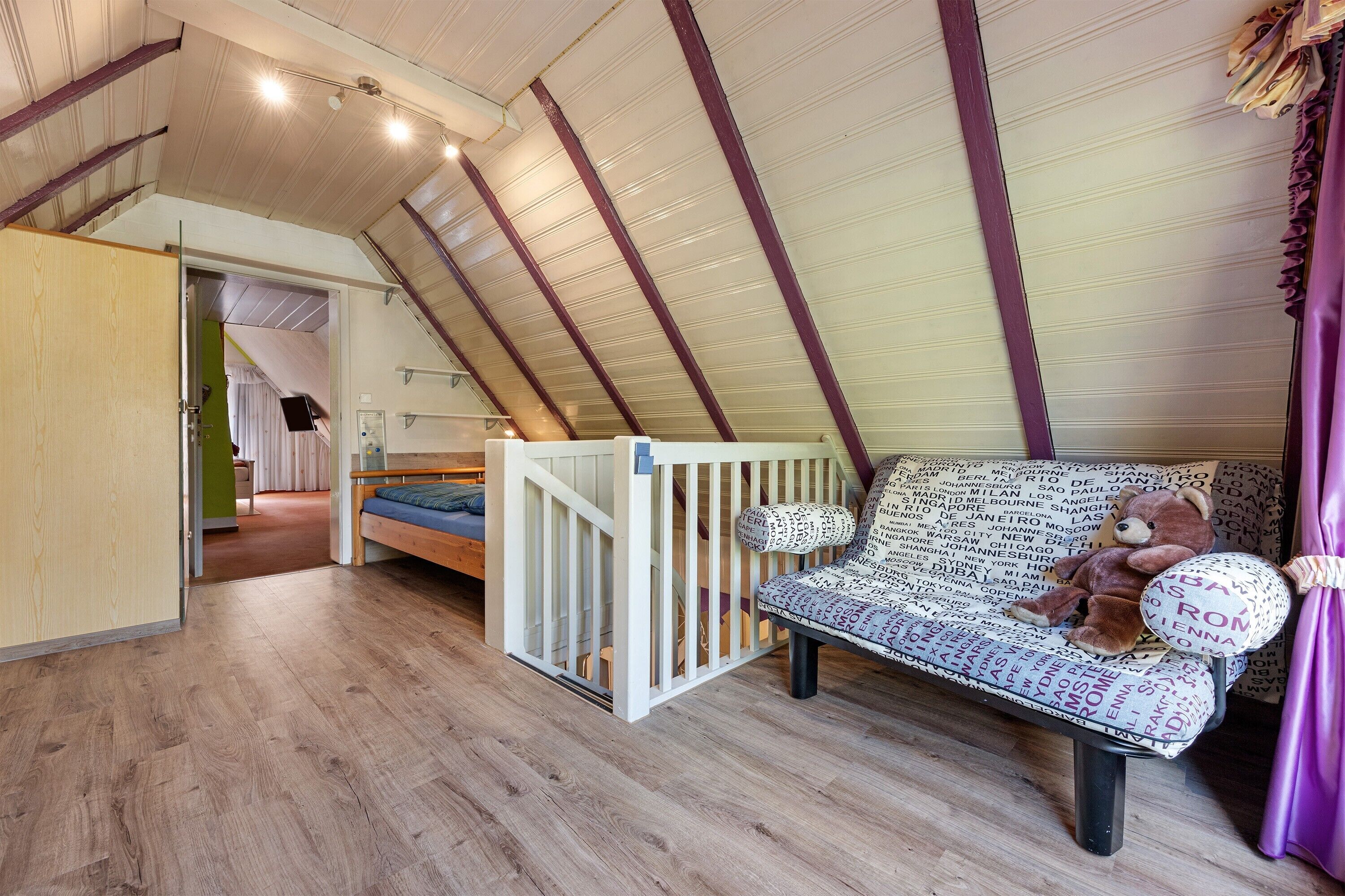 Une chambre à coucher aménagée dans un espace ouvert, avec un lit superposé, un canapé agrémenté de coussins à motifs et un ours en peluche.