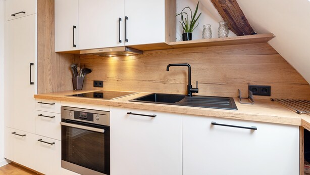 Une cuisine moderne avec des armoires blanches, un plan de travail en bois, un évier noir et un four encastré.