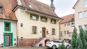Un bâtiment avec un escalier menant à une porte, un petit espace jardin et une voiture garée.