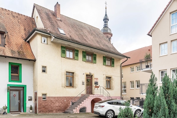 Un bâtiment avec un escalier menant à une porte, un petit espace jardin et une voiture garée.